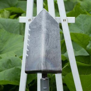 Metal shovel head with green leaves background.