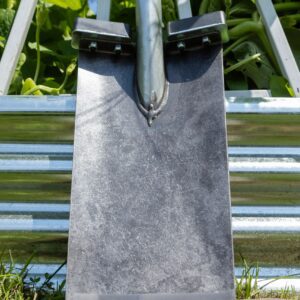 Shovel against metal fence and green plants.