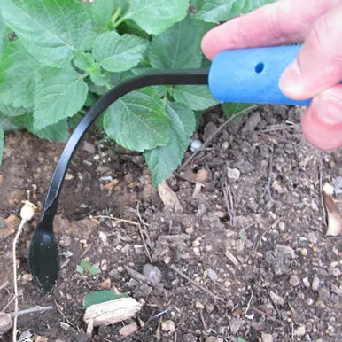 Hand using small hoe in garden soil