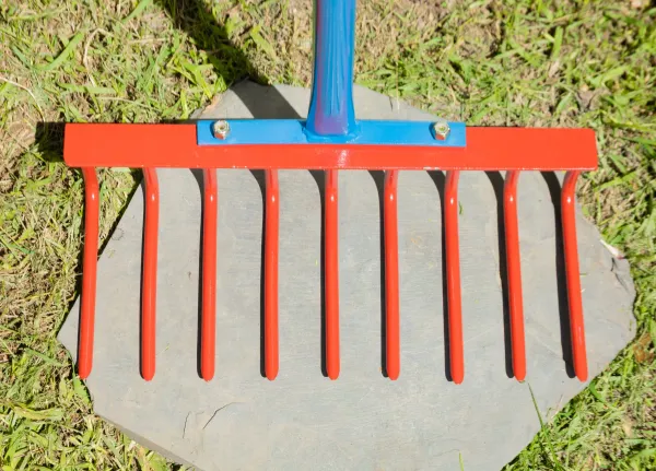 Red metal garden rake on flat stone