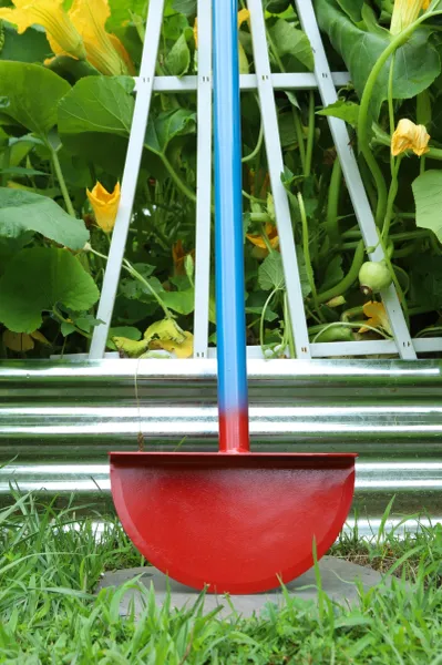 Red half-moon garden shovel against foliage