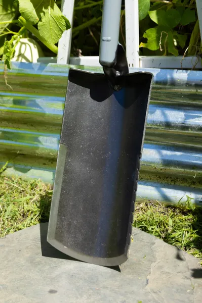 Black garden soil scoop leaning against planter
